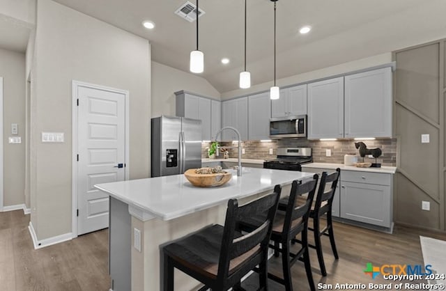 kitchen featuring tasteful backsplash, stainless steel appliances, an island with sink, and a kitchen bar