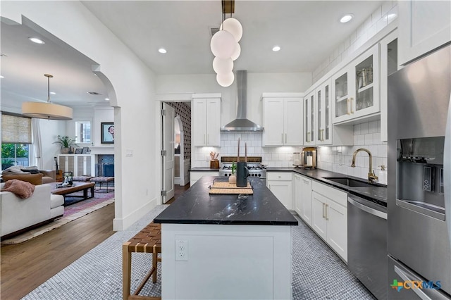 kitchen with wall chimney exhaust hood, sink, hanging light fixtures, appliances with stainless steel finishes, and white cabinets