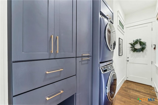 laundry area featuring cabinets, stacked washing maching and dryer, and dark hardwood / wood-style flooring