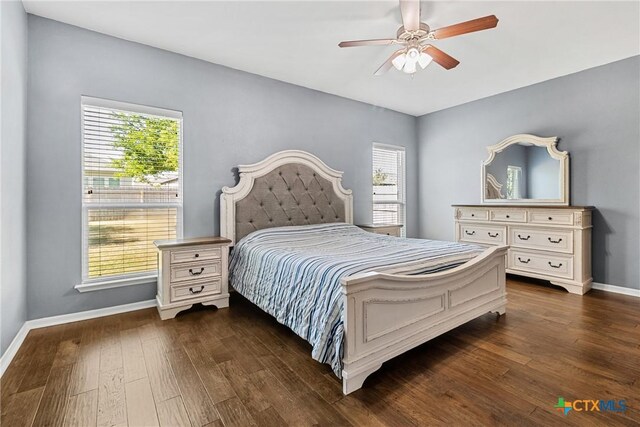 bedroom with dark wood-type flooring, baseboards, multiple windows, and a ceiling fan