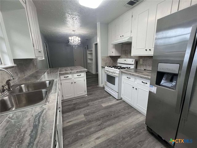 1818 Travis Ave, Victoria, TX 77901 - kitchen featuring stainless steel fridge, white gas range, under cabinet range hood, white cabinets, and a textured ceiling
