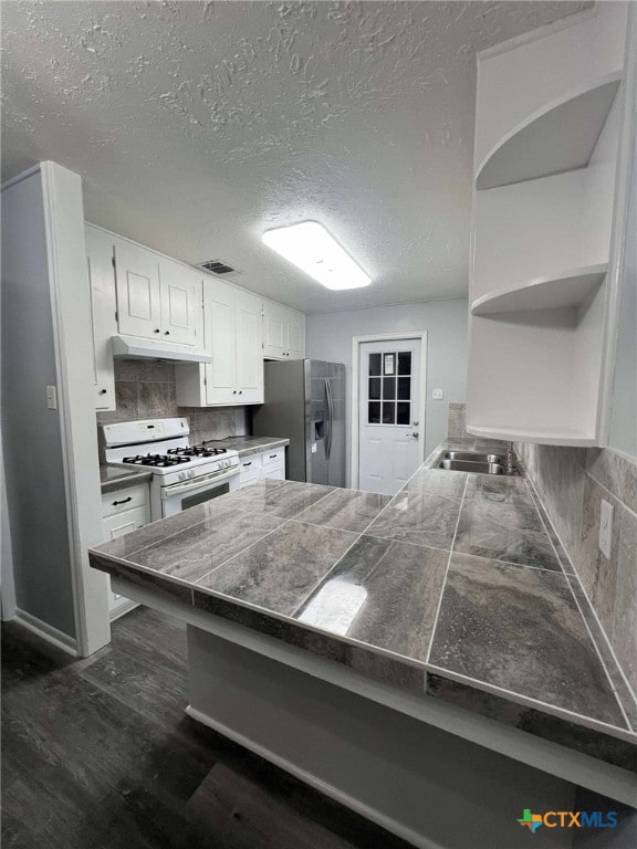 1818 Travis Ave, Victoria, TX 77901 - kitchen with white gas stove, stainless steel fridge with ice dispenser, tile counters, under cabinet range hood, and a peninsula