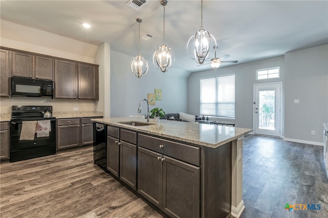 kitchen with dark wood-type flooring, black appliances, sink, an island with sink, and decorative light fixtures