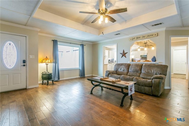 living room featuring ceiling fan, wood-type flooring, a tray ceiling, and ornamental molding