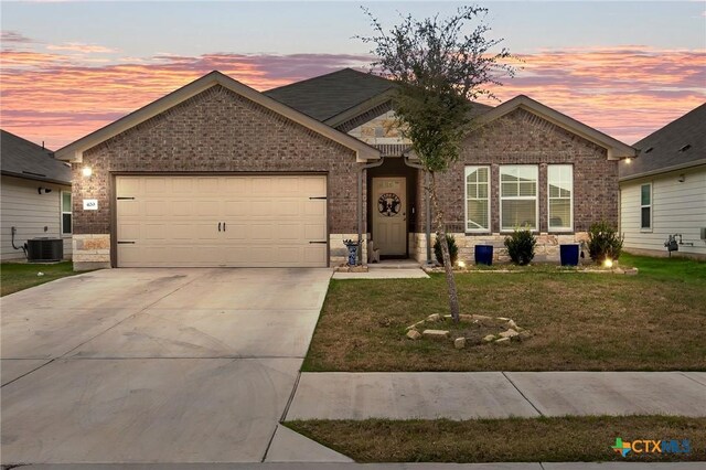 view of front of home with central AC unit, a garage, and a yard