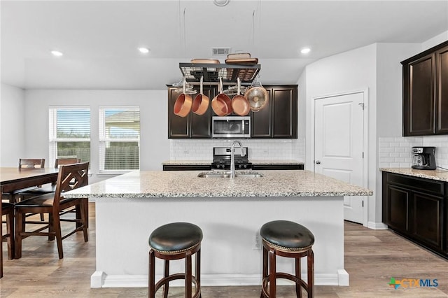 kitchen featuring a center island with sink, sink, light wood-type flooring, appliances with stainless steel finishes, and light stone counters