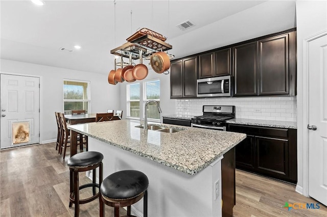 kitchen with a kitchen island with sink, sink, decorative backsplash, light wood-type flooring, and stainless steel appliances