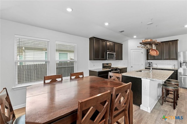 kitchen featuring sink, stainless steel appliances, tasteful backsplash, light stone counters, and a kitchen island with sink