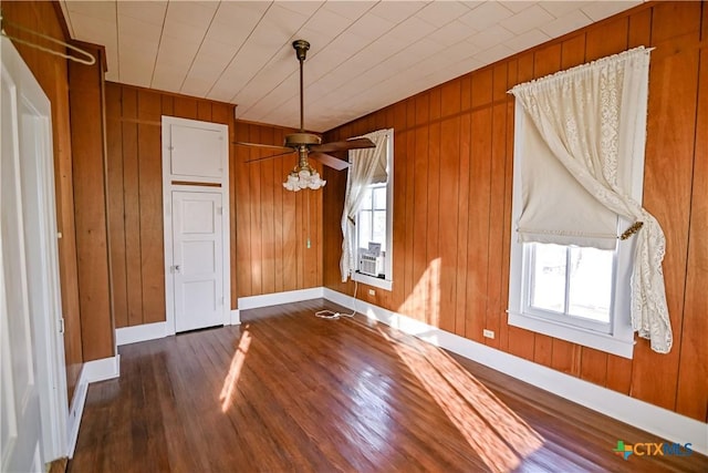 unfurnished dining area featuring dark wood-type flooring, plenty of natural light, ceiling fan, and wooden walls