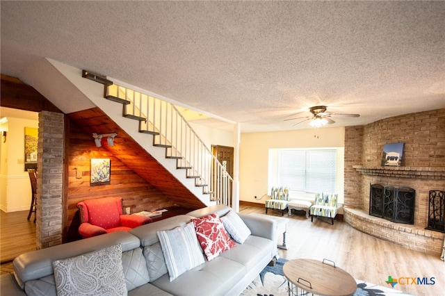 living room featuring a brick fireplace, wood-type flooring, a textured ceiling, and ceiling fan