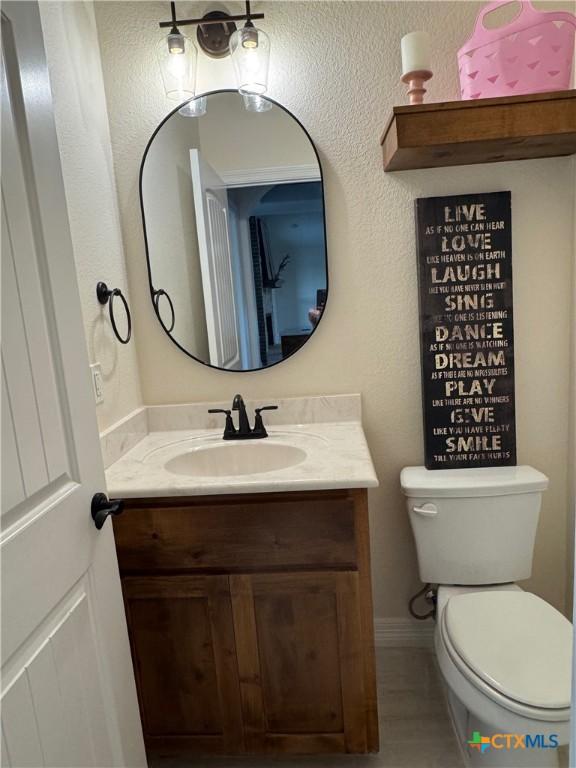 half bath with baseboards, vanity, and toilet