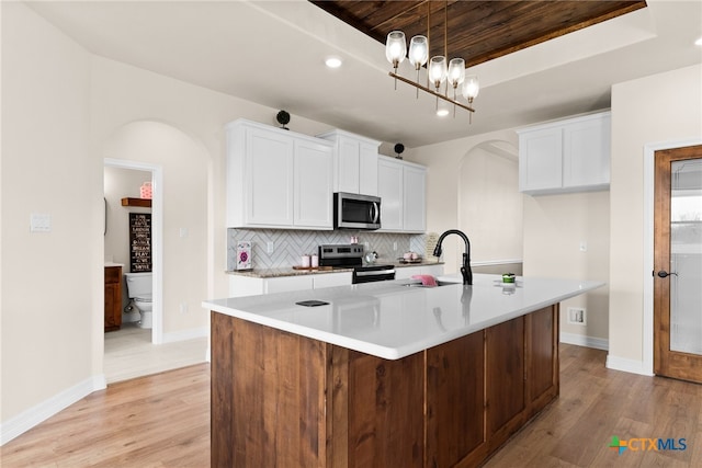 kitchen with arched walkways, a tray ceiling, stainless steel appliances, backsplash, and a sink