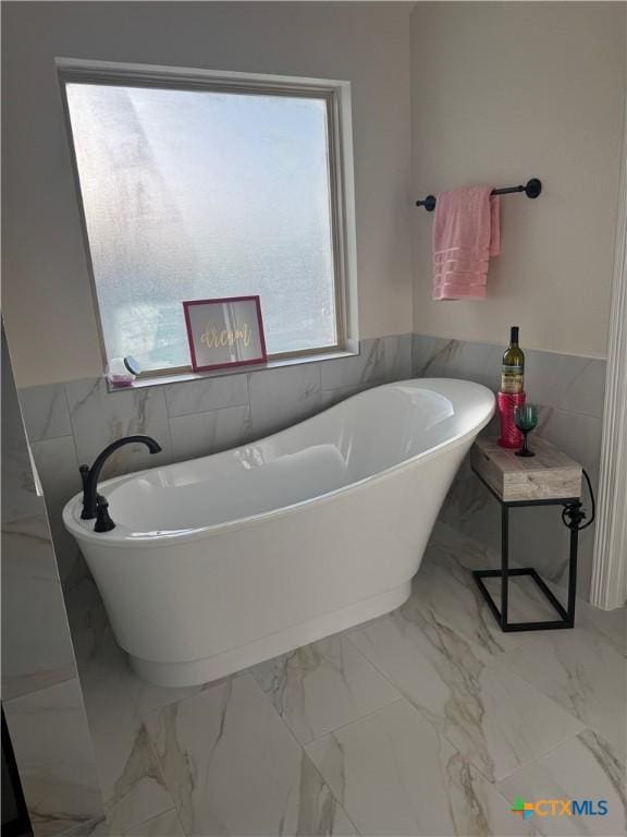 full bath featuring marble finish floor, wainscoting, a freestanding tub, and tile walls