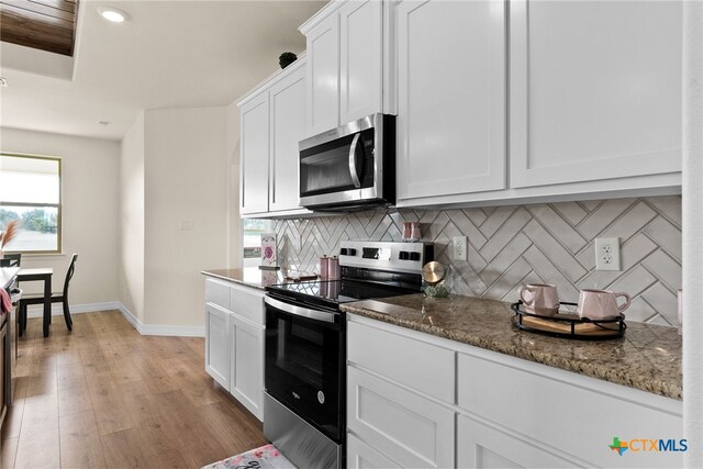 kitchen with light stone countertops, backsplash, a raised ceiling, sink, and white cabinetry