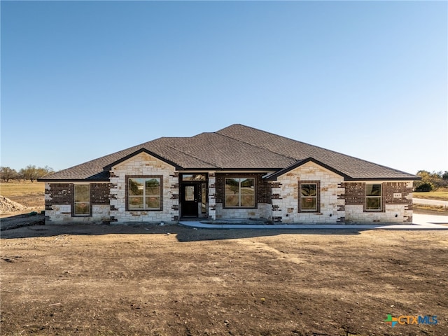 view of front of property featuring stone siding and roof with shingles