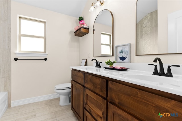 full bathroom with toilet, double vanity, baseboards, and a sink