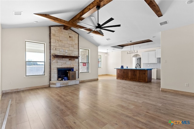 unfurnished living room featuring a fireplace, lofted ceiling with beams, light hardwood / wood-style floors, and a wealth of natural light