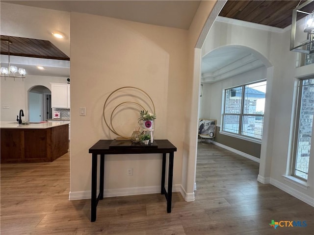 hallway with light wood-type flooring, an inviting chandelier, baseboards, and arched walkways