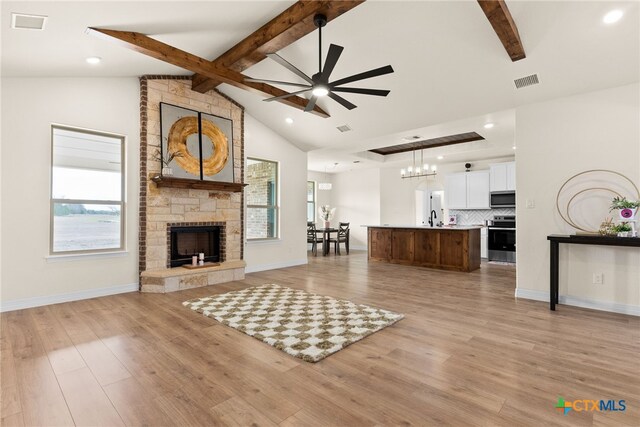 unfurnished living room featuring light wood-type flooring, lofted ceiling with beams, a stone fireplace, and ceiling fan