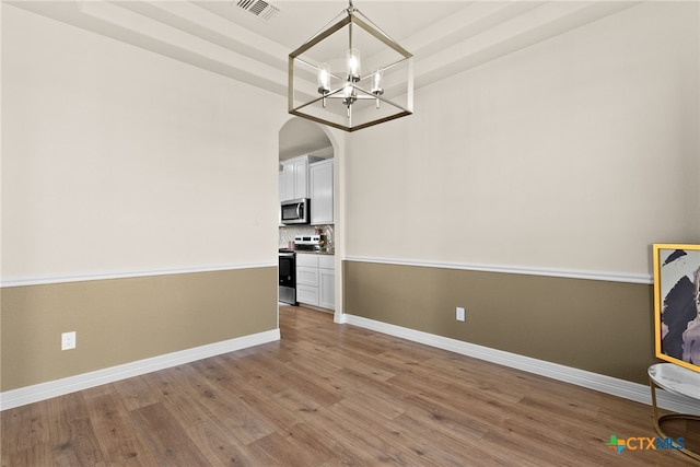 unfurnished dining area featuring arched walkways, wood finished floors, baseboards, and an inviting chandelier