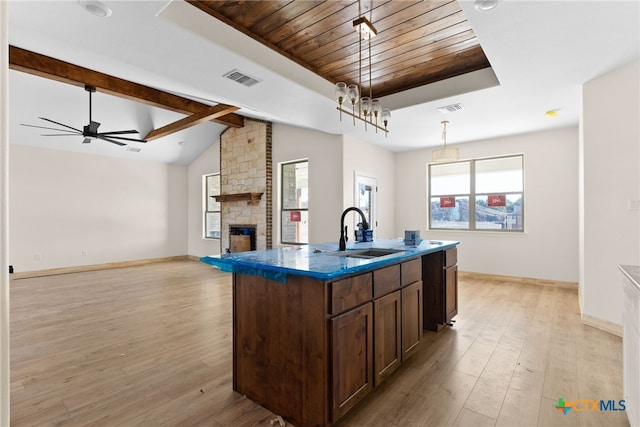 kitchen with a fireplace, sink, an island with sink, and light wood-type flooring