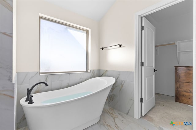 bathroom with lofted ceiling, a bath, and tile walls