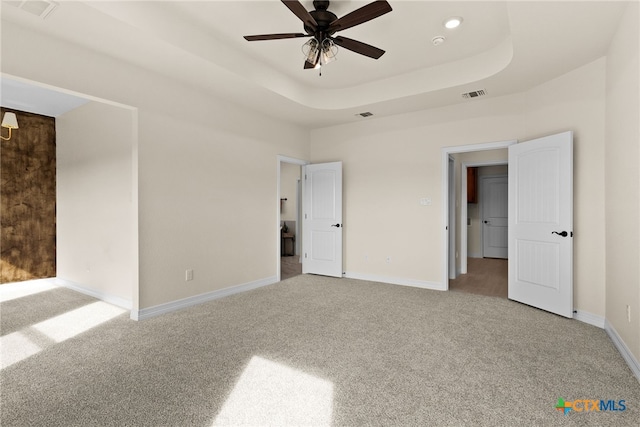 unfurnished bedroom featuring carpet floors, a tray ceiling, visible vents, and baseboards