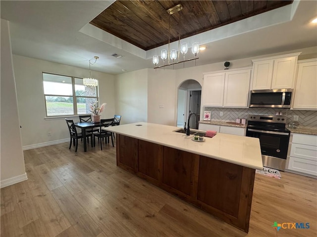 kitchen featuring arched walkways, appliances with stainless steel finishes, backsplash, and a raised ceiling