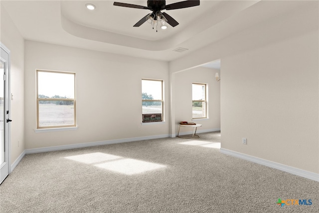 empty room featuring a tray ceiling, carpet, visible vents, and baseboards