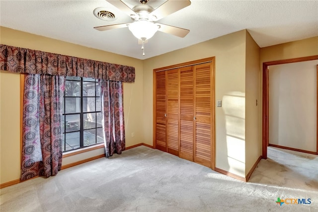 unfurnished bedroom with ceiling fan, a closet, light colored carpet, and a textured ceiling