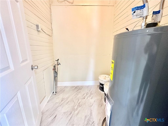 laundry room with wooden walls, baseboards, marble finish floor, and electric water heater