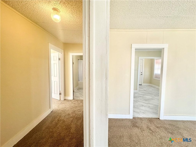 hallway featuring baseboards, carpet floors, and a textured ceiling