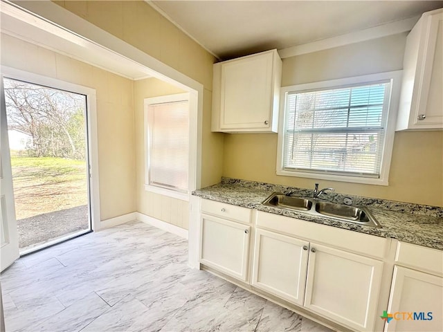 kitchen with marble finish floor, a sink, light stone counters, white cabinets, and baseboards