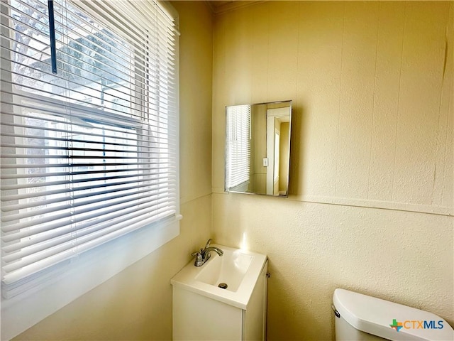 half bathroom with toilet, vanity, and a textured wall