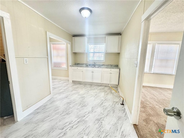 kitchen featuring white cabinets, a textured ceiling, crown molding, and a sink