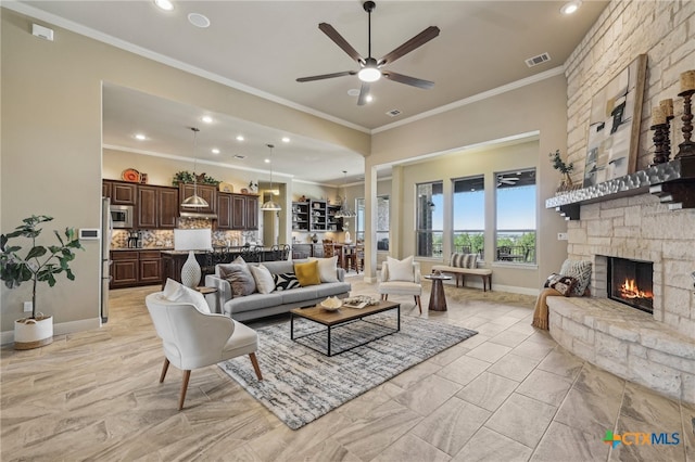 living area featuring visible vents, ornamental molding, a ceiling fan, a stone fireplace, and baseboards