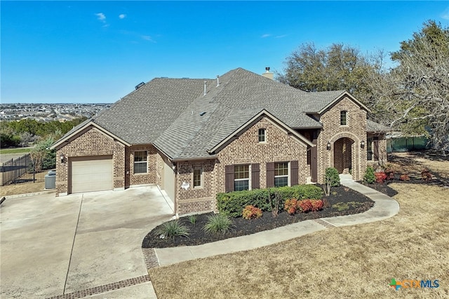 french country home featuring an attached garage, brick siding, fence, driveway, and roof with shingles