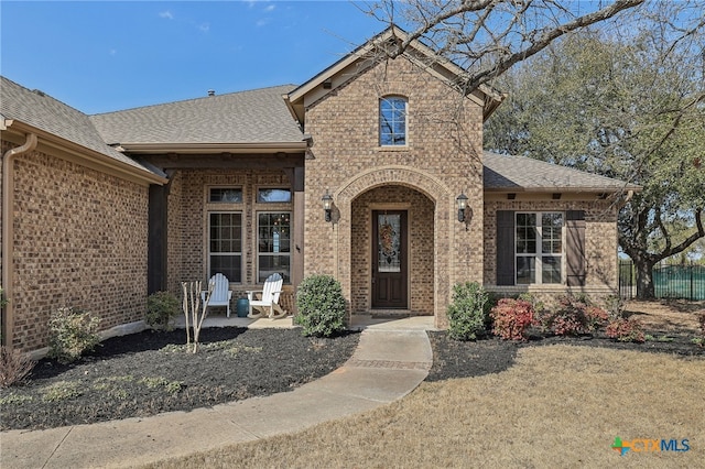 view of front of property featuring a shingled roof, fence, and brick siding