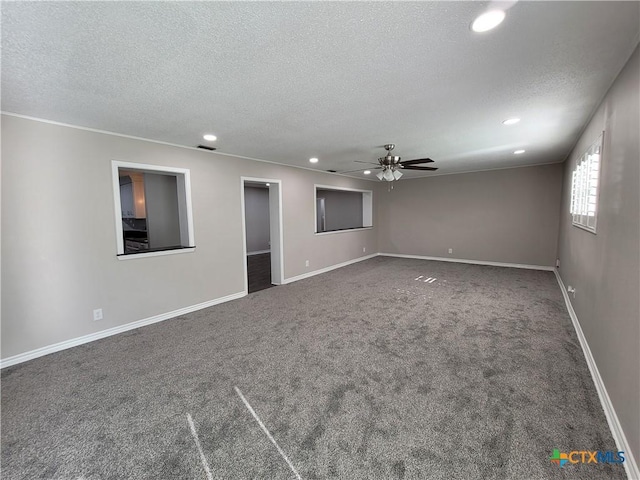 empty room featuring ceiling fan, a textured ceiling, and dark carpet