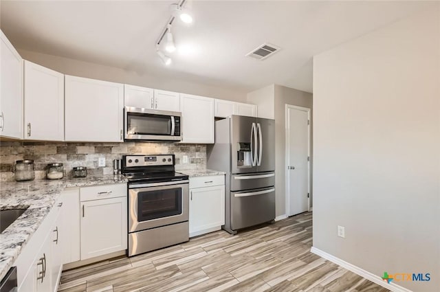 kitchen featuring appliances with stainless steel finishes, white cabinets, decorative backsplash, light stone counters, and light wood-type flooring