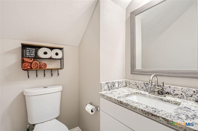 bathroom featuring vanity, a textured ceiling, vaulted ceiling, and toilet