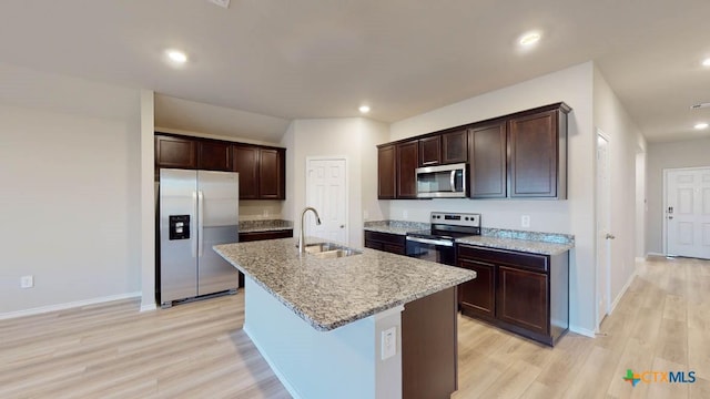 kitchen with sink, a kitchen island with sink, light stone counters, stainless steel appliances, and light wood-type flooring