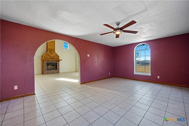 tiled spare room with a brick fireplace, ceiling fan, and a textured ceiling