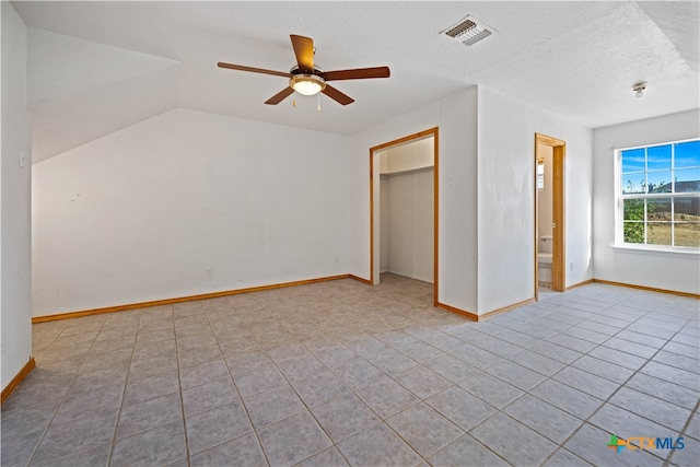 unfurnished bedroom featuring a closet, a textured ceiling, light tile patterned floors, lofted ceiling, and ceiling fan