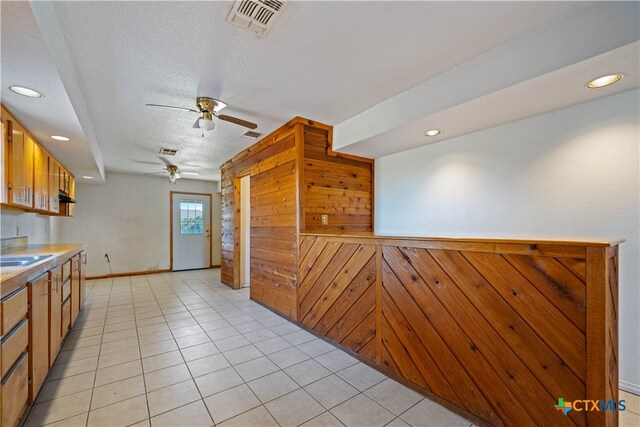 kitchen featuring wood walls, a textured ceiling, sink, light tile patterned floors, and ceiling fan