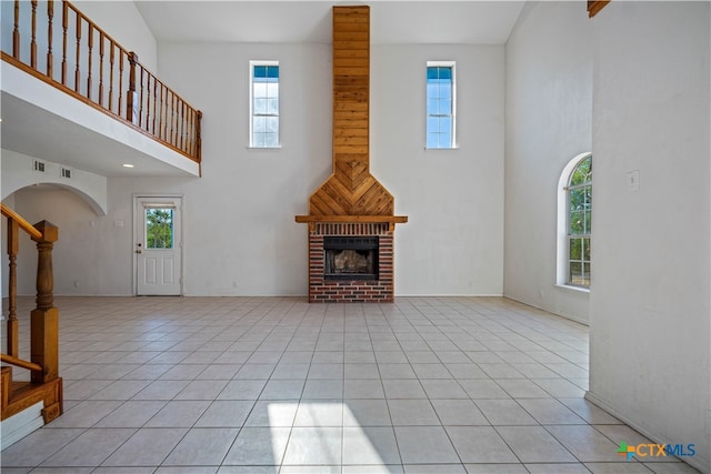 unfurnished living room with a fireplace, light tile patterned floors, and a towering ceiling