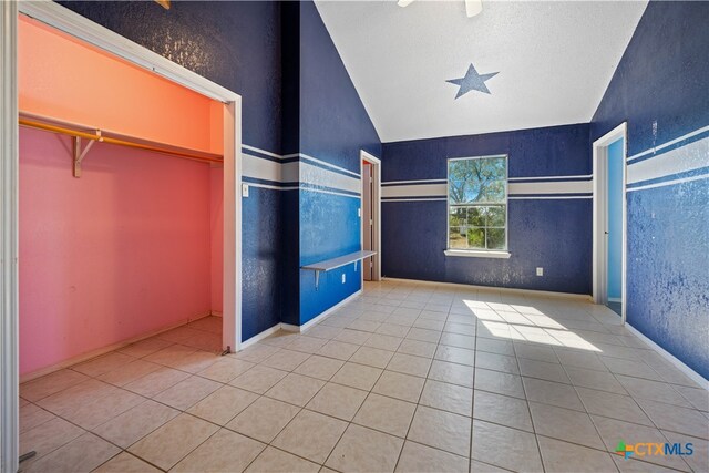 unfurnished bedroom with light tile patterned floors, vaulted ceiling, and a closet