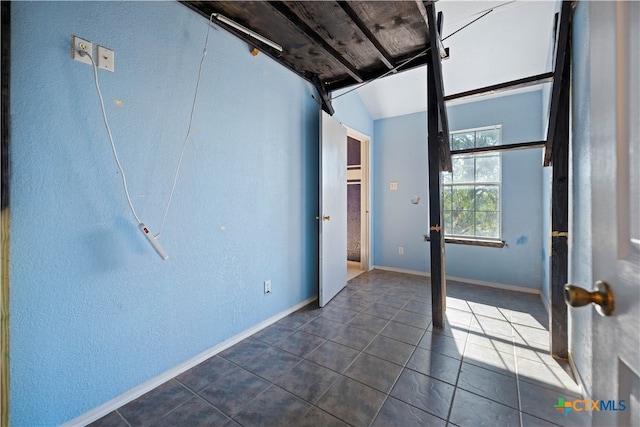 empty room featuring dark tile patterned floors and vaulted ceiling