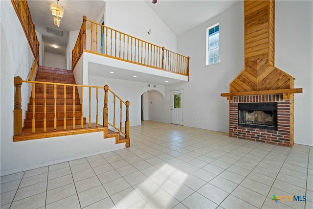 unfurnished living room with a brick fireplace, a towering ceiling, and light tile patterned flooring