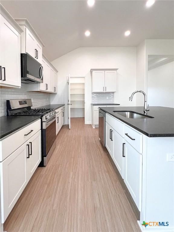116 Raindance Ct, Victoria, TX 77904 - kitchen featuring appliances with stainless steel finishes, dark countertops, lofted ceiling, tasteful backsplash, and light wood-style floors